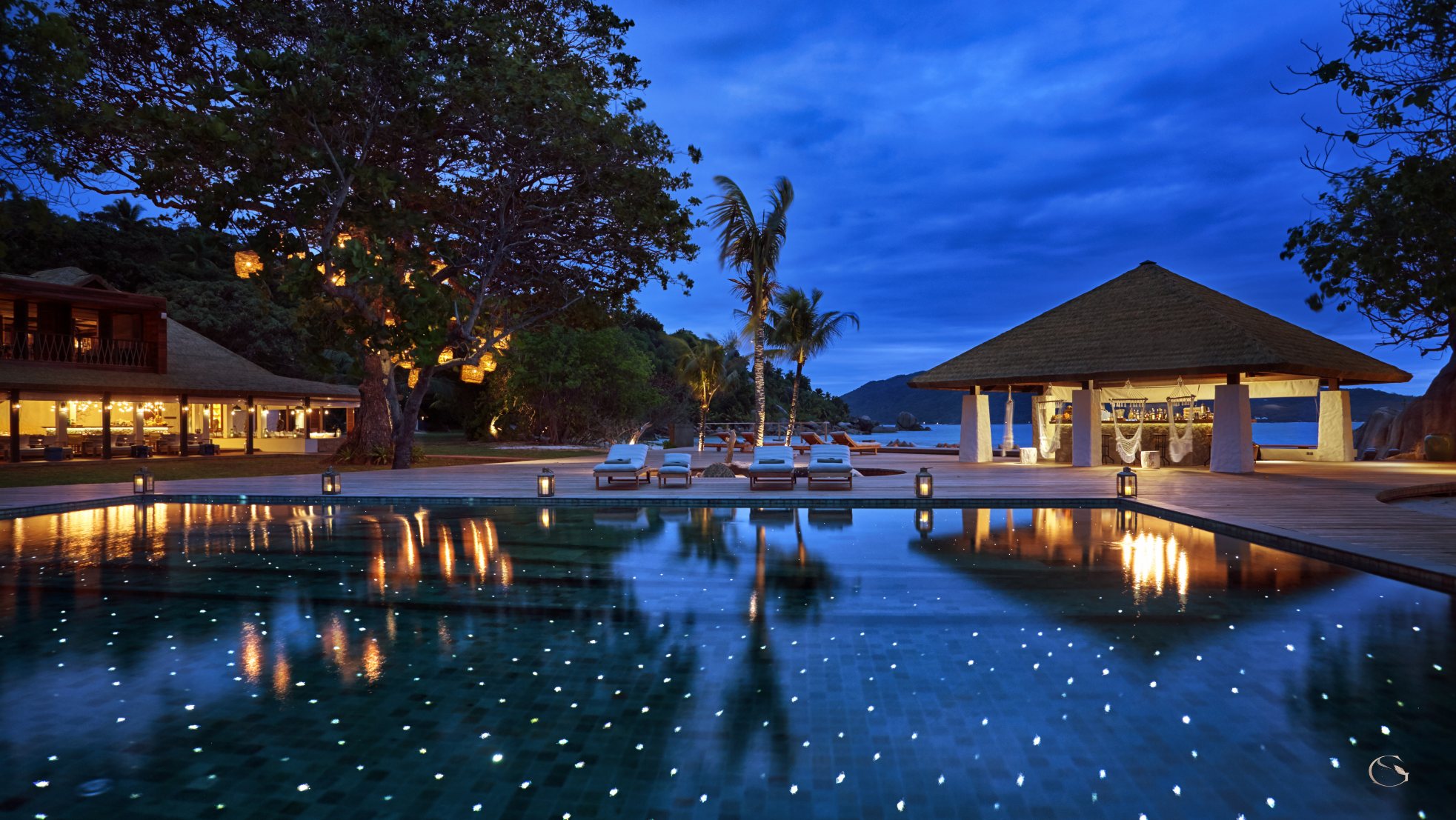 Main pool and Koko Bar lit at dusk, Six Senses Zil Pasyon LuxurySafariLodges.com